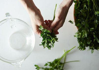 A person is cooking with parsley by putting it into a glass bowl.