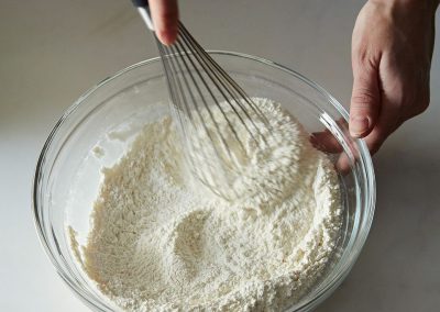 A person is whisking flour into a bowl while cooking.