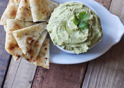 A bowl of guacamole and pita chips on a wooden table, perfect for cooking with cilantro.