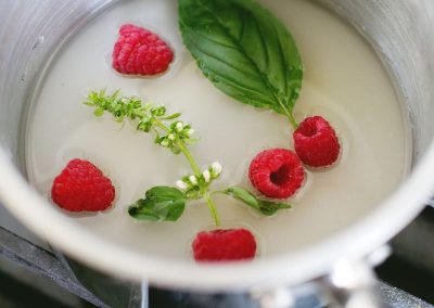 Cooking with basil, a pot filled with raspberries and basil on a stove.