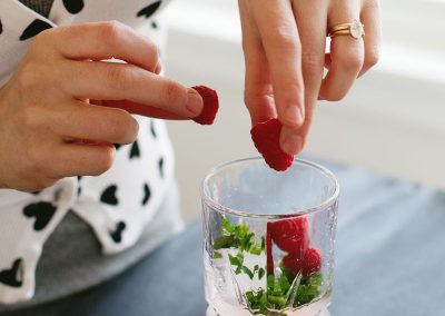 A woman is adding raspberries to a glass of water, incorporating a refreshing twist to her beverage.