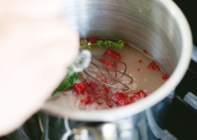 A person stirring a pot of liquid with berries in it, cooking with basil.