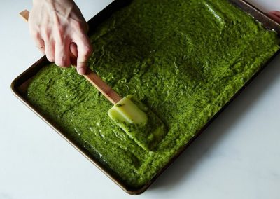 A person cooking with parsley, squeezing green pesto onto a baking sheet.