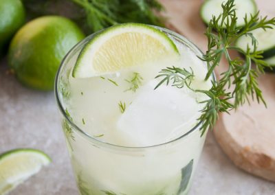 A refreshing drink with cucumber and lime infused with the aromatic touch of dill, showcased on a cutting board.