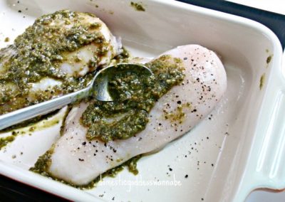 Two chicken breasts with mint pesto sauce in a baking dish.