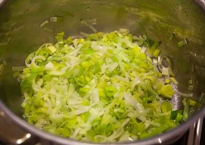 A pot with onions, celery, and parsley in it.