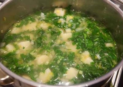 Cooking a flavorful pot of soup with potatoes and greens, seasoned with parsley.